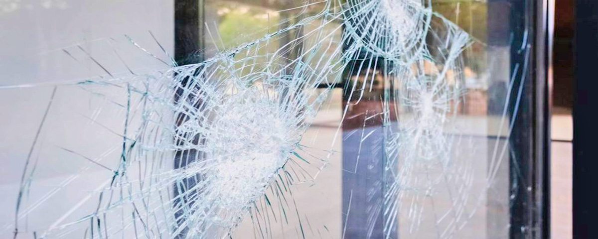 Close-up of a shattered glass door with multiple cracks, demonstrating the impact of a break-in. Security window film can help protect against such damage